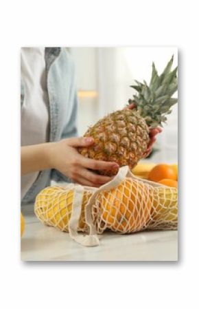 Woman taking pineapple out from string bag at light marble table, closeup