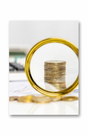 Magnifying glass focuses on stacked coins with calculator nearby in a financial setting