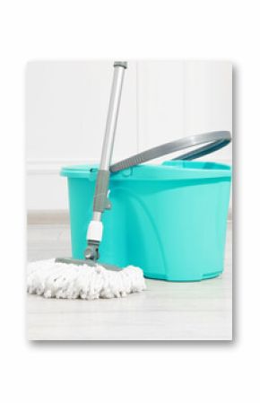 String mop and bucket on wooden floor near white wall