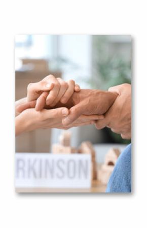 Senior man suffering from Parkinson syndrome with woman holding hands at home, closeup