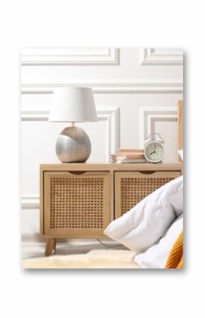 Bedside table with lamp, alarm clock and books near bed indoors