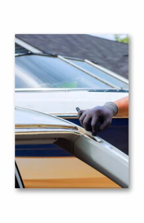 Worker works on car in driveway, repairing vehicle while auto sits nearby under replacement damaged windshield