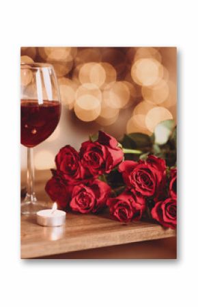 Romantic Dinner. Bouquet of flowers lying on the table, selective focus on bunch of roses, two glasses of red wine and candles on the wooden desk. Date concept, blurred background, banner, copy space