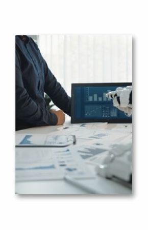 A modern office setting showcases a business meeting where human participants collaborate with a robotic arm, analyzing data and financial reports displayed on screens.Noogenesis
