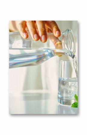 Hand pouring pure fresh water into a glass. Healthy morning hydration habit for a detox diet. Wellness and health lifestyle concept with lemon and mint. 