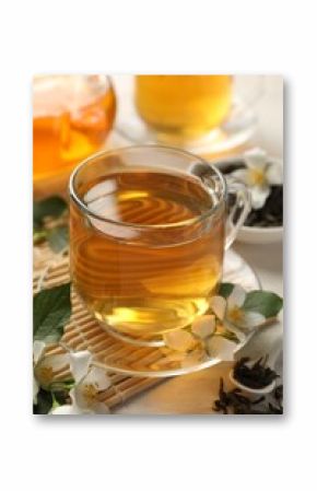 Tasty jasmine tea in cup, dry leaves and flowers on white wooden table, closeup