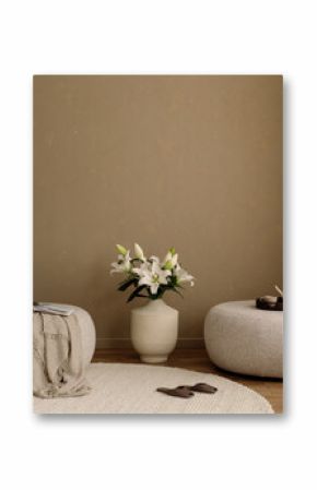 Elegant living space with beige sofa, large vase of white lilies, round pouf and textured neutral wall. Copy space.