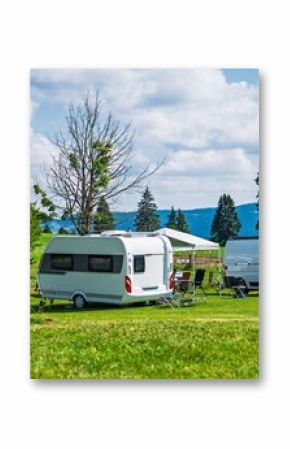 A scenic camping spot with a caravan, car, and camper van on a green meadow beneath a blue sky with fluffy clouds, ideal for travel and outdoor adventure themes.