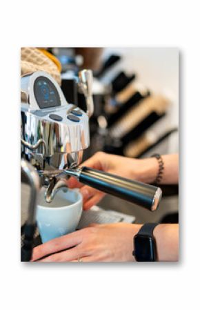 Barista preparing espresso with a portafilter in a modern coffee machine. White cup on drip tray, smartwatch and bracelet visible, coffee shop background blurred