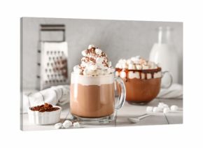 Glass cups of hot cocoa drink with whipped cream and marshmallows on white tile table