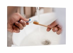 Hands putting toothpaste on a bamboo toothbrush for daily dental hygiene