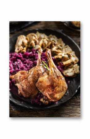 Portion of roast duck leg red cabbage homemade dumplings on plate and red wine on the background