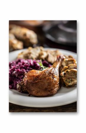 Portion of roast duck leg red cabbage homemade dumplings on plate and red wine on the background