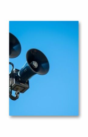 Alarm siren and speakers on pole against blue sky