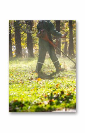 A worker using a string trimmer to maintain a lush green park during autumn sunlight in a vibrant outdoor setting