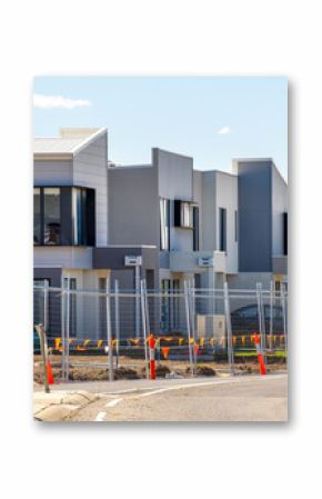 A development of new modern townhouses or multi-unit residences in an outer suburb in Australia, under construction with temporary fencing, safety cones, and unfinished landscaping