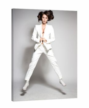 Awesome caucasian attractive joyful happy sexy dance model is jumping in studio wearing white suit on gray background