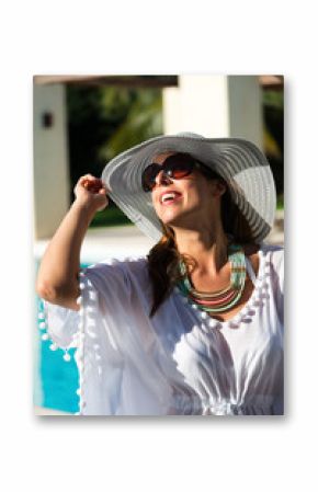 Fashion woman having fun and relaxing at luxury hotel resort spa pool. Fashionable caucasian model wearing sun hat, sunglasses and white summer dress.