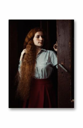 Pretty ginger girl with long hair and freckles standing at the old doors