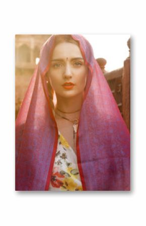 Close-up portrait of a beautiful young woman with a gorgeous bindi on her forehead. Long blonde hair is tangled in hairstyle. She is covered with a beautiful purple silk scarf with small prints.