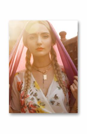 Close-up portrait of a beautiful young woman with a gorgeous bindi on her forehead. Long blonde hair is tangled in hairstyle. She is covered with a beautiful purple silk scarf with small prints.