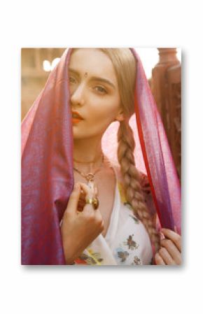 Close-up portrait of a beautiful young woman with a gorgeous bindi on her forehead. Long blonde hair is tangled in hairstyle. She is covered with a beautiful purple silk scarf with small prints.