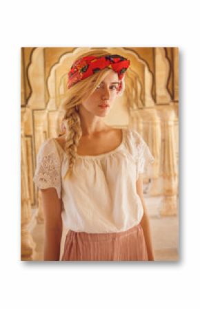 Close-up portrait of a beautiful young woman with a gorgeous scarf on her head. She is dressed in a pretty white shirt and captured between old pillars.