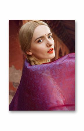 Close-up portrait of a beautiful young woman with a gorgeous bindi on her forehead. Long blonde hair is tangled in hairstyle. She is covered with a beautiful purple silk scarf with small prints.