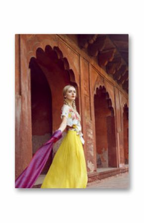 A beautiful young woman walking with a gorgeous bindi on her forehead. Long blonde hair is tangled in wonderful hairstyle. She is palying with a beautiful purple silk scarf with small prints.