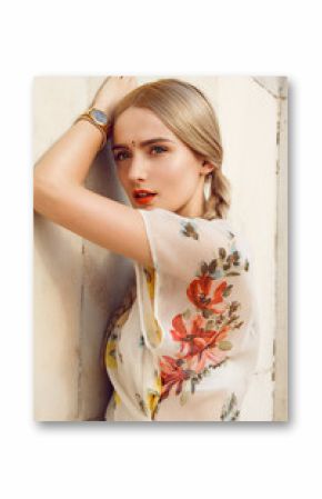 Close-up portrait of a beautiful young woman with gorgeous bindi on her forehead. Long blonde hair is tangled in wonderful hairstyle. And she is dressed in a pretty dress with floral print.