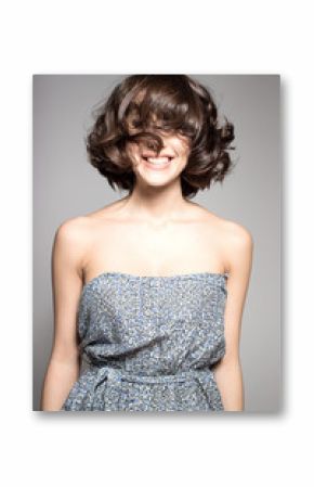 Awesome caucasian attractive joyful happy sexy female model is shaking head with brunette hair in studio wearing nice dress, isolated on gray background