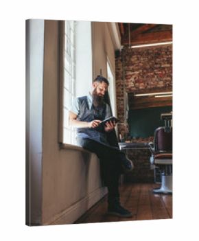 Young barber at his barbershop using digital tablet