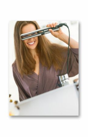 Happy young woman looking through hair straightener in bathroom
