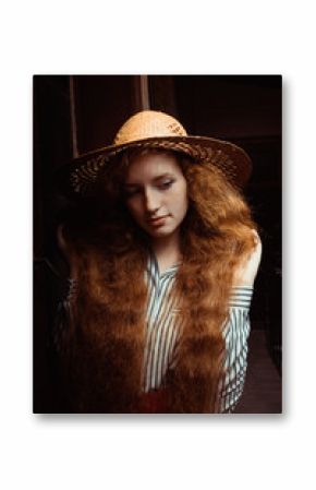 Attractive young red haired woman with freckles in straw hat posing in passage