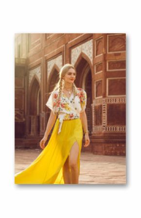 A beautiful young woman walking with a gorgeous bindi on her forehead. Long blonde hair is tangled in wonderful hairstyle. And she is dressed in a pretty shirt with floral print and yellow skirt.