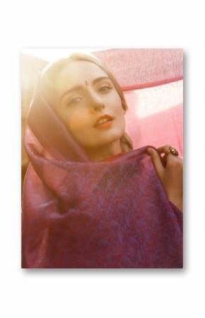 Close-up portrait of a beautiful young woman with a gorgeous bindi on her forehead. Long blonde hair is tangled in hairstyle. She is covered with a beautiful purple silk scarf with small prints.