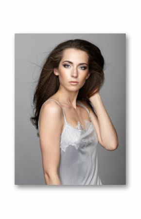 Beauty portrait of young woman. Brunette girl with long disheveled flying hair and day female makeup on gray background