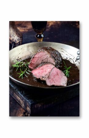 Traditional German venison roast with juniper berry and rosemary in spicy red wine sauce served as close-up in a frying pan