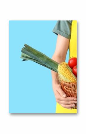 Female farmer with wicker basket full of different vegetables on light blue background with space for text