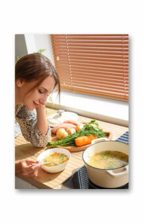 Young woman eating chicken soup in kitchen