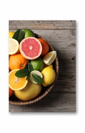 Different fresh citrus fruits and leaves in wicker basket on wooden table, top view. Space for text