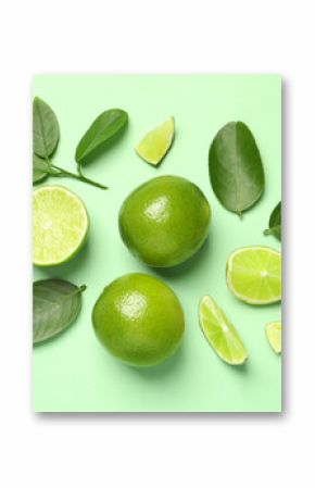 Whole and cut fresh ripe limes with leaves on light green background, flat lay