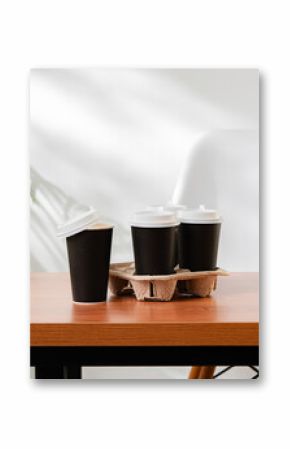 Takeout coffee cups placed on a wooden table next to a green indoor plant