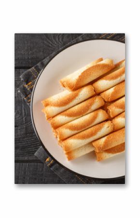 Cigarettes russes or russian cigarettes is a baked thin waffle rolls closeup on the plate on the table. Horizontal top view from above