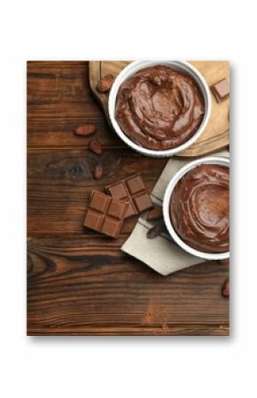 Tasty pudding in bowls, pieces of chocolate and cocoa beans on wooden table, flat lay. Space for text