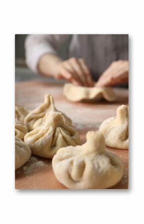 Woman making khinkali on table in kitchen, closeup