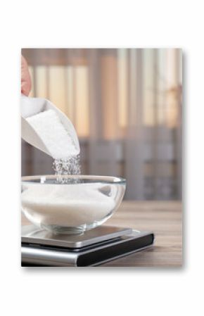 Woman adding sugar into bowl and digital kitchen scale at wooden table indoors, closeup. Space for text