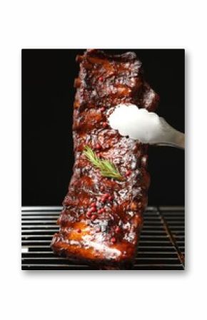 Taking delicious roasted pork ribs with tongs from grill on black background, closeup