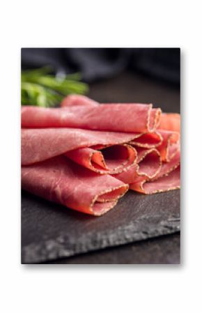 Sliced beef pastrami on cutting board on black table.