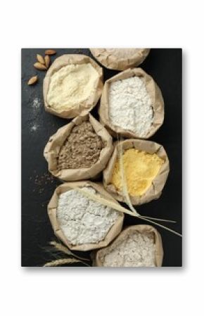 Different types of flour in paper bags on black table, flat lay